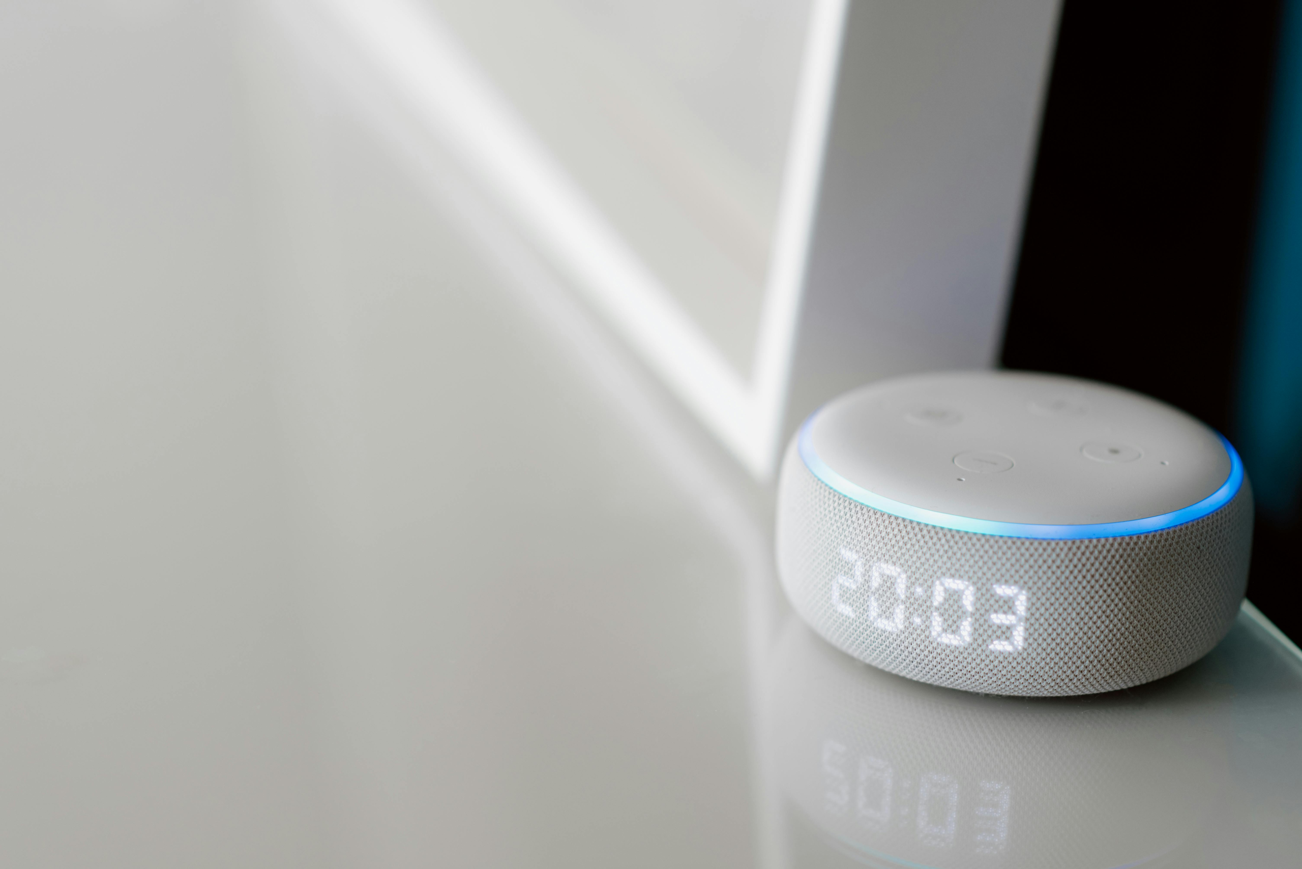 Close-up of a smart speaker with a digital clock display on a minimalist surface.